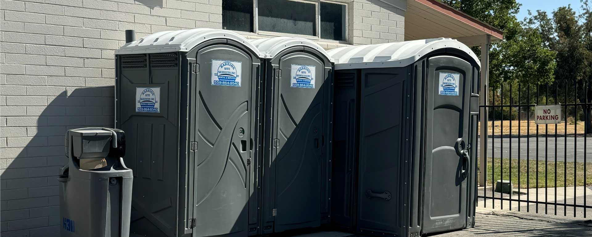 A row of portable toilets including an ADA-compliant unit and a standalone handwash station for complete public site compliance