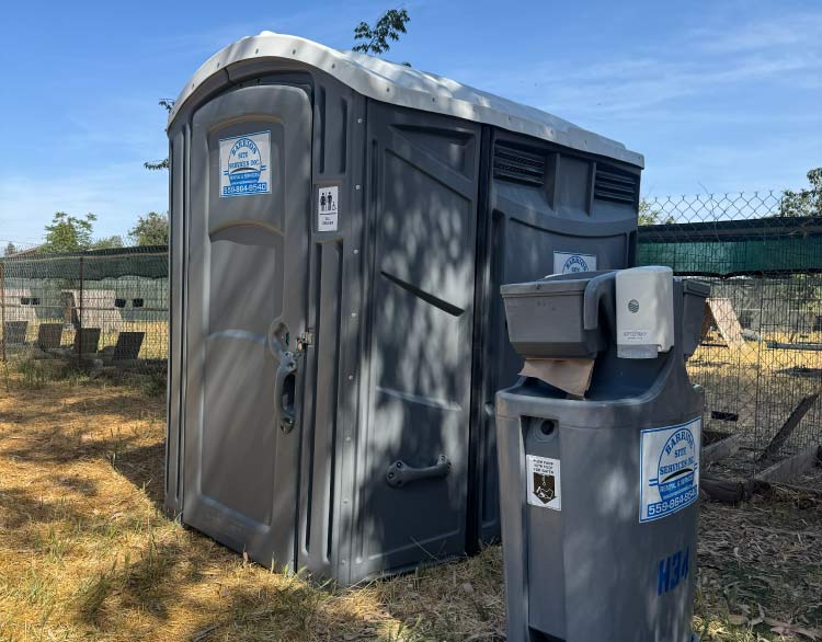 Wheelchair-accessible ADA unit from Barrios Site Services Inc. placed alongside a standalone handwash station to meet public event compliance requirements.