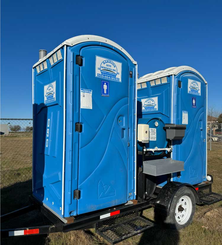 A rear-view of a blue double-trailer mobile toilet rentals showing the holding tanks and handwash station assembly for mobile job site sanitation.