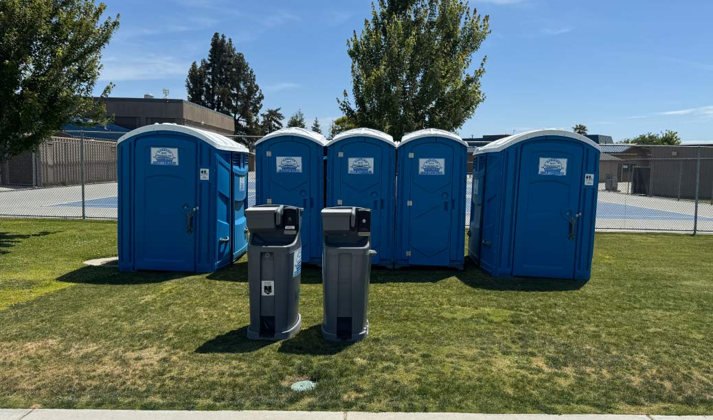 Fleet of blue standard portable toilets from Barrios Site Services Inc. lined up at an outdoor sports complex to provide sanitary facilities for public events