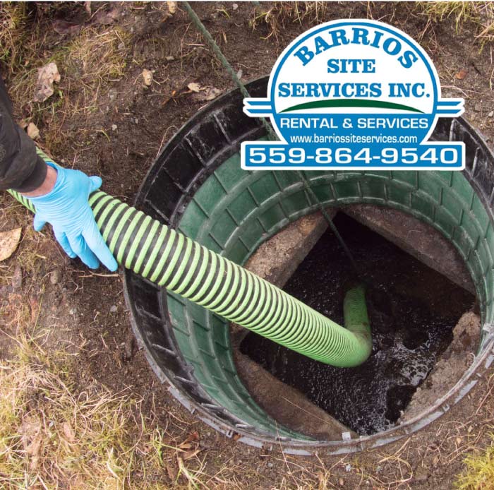 High-powered vacuum hose being used by a professional in blue gloves to perform deep septic pumping and sludge removal from a residential tank.