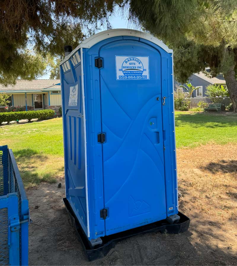 Barrios Site Services blue standard portable toilet rental featuring a 3-roll toilet paper dispenser and seat cover dispenser, professionally maintained for Fresno and Madera county construction sites.