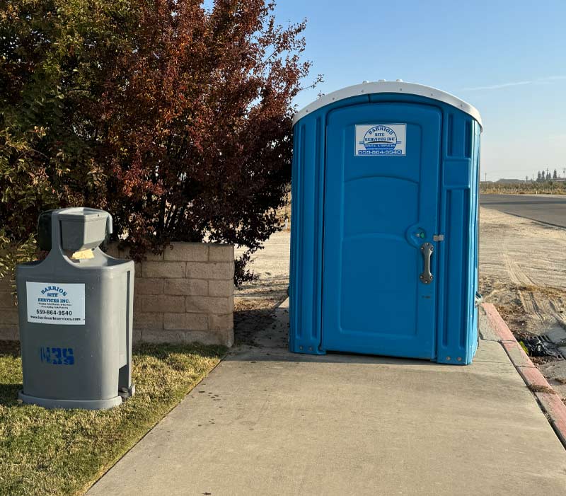 Barrios Site Services ADA-compliant portable restroom with a ground-level entrance for easy wheelchair access, accompanied by a standalone foot-pump operated handwash station.