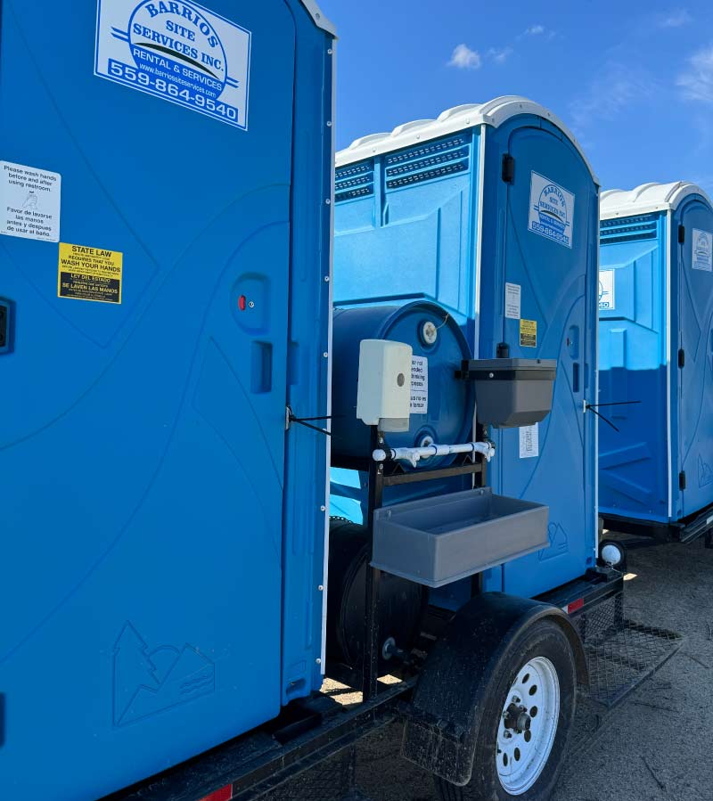 Clean Barrios Site Services portable toilets in Fresno with custom-fabricated external handwash stations featuring metal frames and water drums for G.A.P. compliant agricultural sanitation.