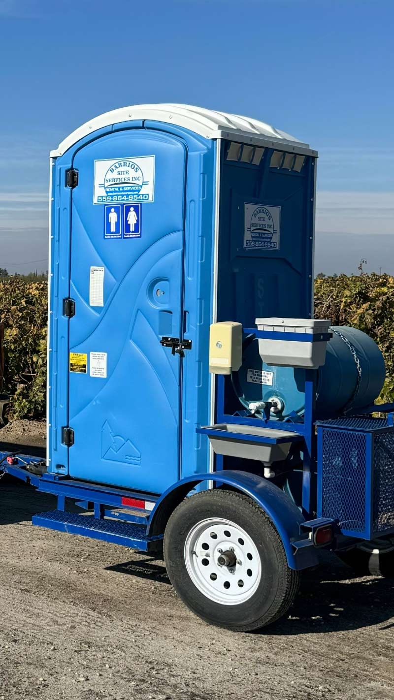 Custom-fabricated Barrios Site Services towable restroom unit featuring a specialized external handwash station with water drum and metal frame, ideal for G.A.P. compliant sanitation in vineyards and orchards.